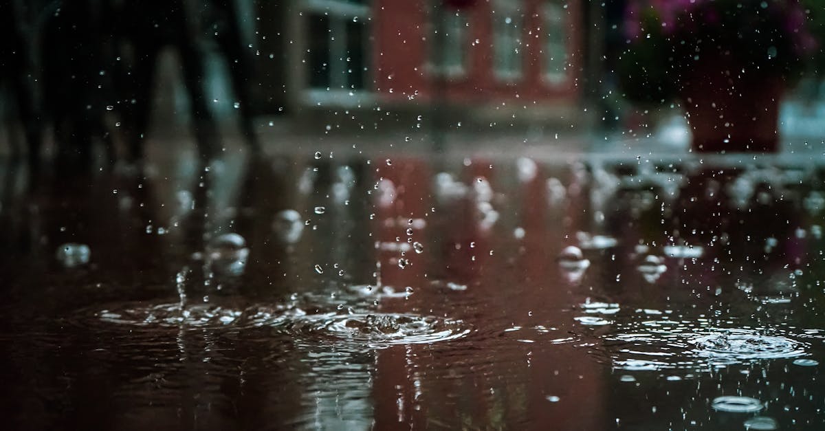 Close-up of raindrops splashing into a puddle, capturing reflections and textures in an outdoor urban setting.